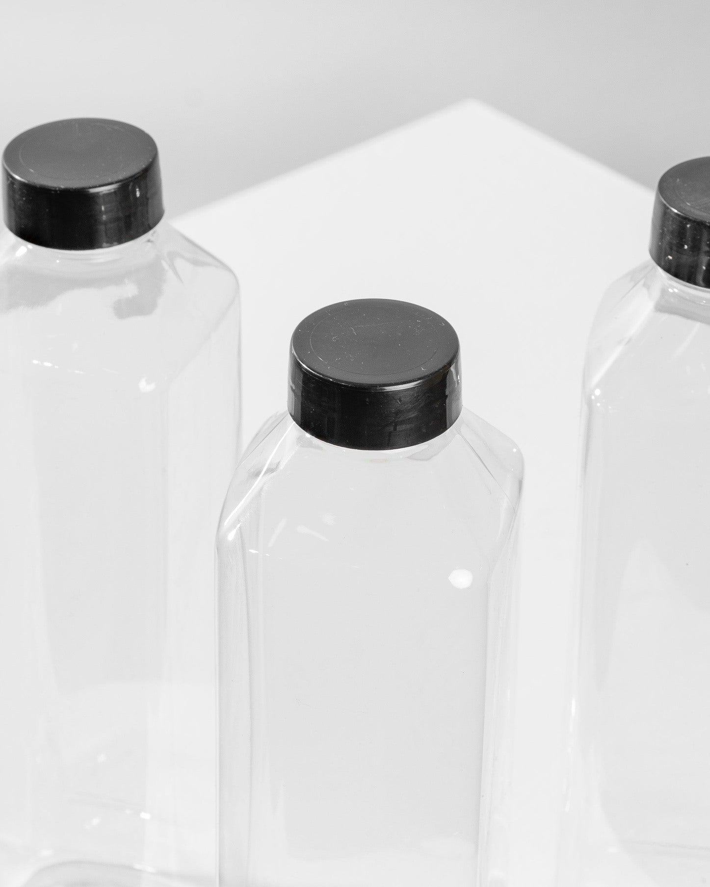 Three clear plastic bottles with black lids on a white background